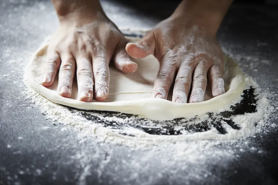 Pizza dough being rolled out on a table